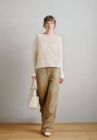 Codzienny strój składający się z jasnobeżowego swetra z dzianiny, szerokich, beżowych spodni i kremowej torebki, na drewnianej podłodze na tle szarej ściany.