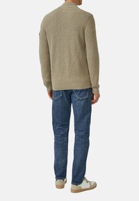 Hellbrauner, strukturierter Cardigan mit Rippmuster; kombiniert mit dunkelblauen Jeans und cremefarbenen Sneakers. Die Ansicht zeigt die Rückseite des Outfits.