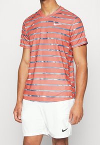 Camiseta deportiva de manga corta a rayas rojas y azules con cuello en V, hecha de una tela ligera. Presenta un pequeño logotipo de Nike en el pecho.