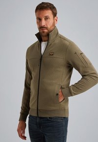 Khaki jumpertje met ritssluiting en een getextureerd bovenpaneel, twee zijzakken en een ritssluiting op de mouw; zachte stof met geribbelde manchetten.