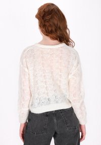 Maglione bianco leggero e lavorato a maglia con una vestibilità ampia, caratterizzato da un motivo testurizzato, un colletto a coste e maniche lunghe. Abbinato a jeans scuri.