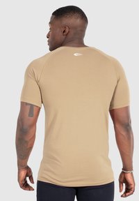 Tan kortärmad t-shirt med en åtsittande design, slät textur och en vit logotyp på baksidan, sedd bakifrån.