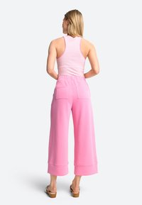 Roze wijde broek met gestructureerde stof, voorzien van een hoge tailleband en twee achterzakken. Gecombineerd met een getailleerde, gestreepte tanktop.