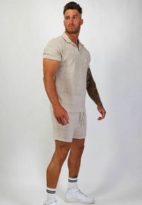 Ljust beige polo och matchande shorts, tillverkade av mjukt tyg. Har en krage, korta ärmar och dragsko i midjan. Bärs med vita sneakers.