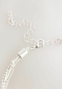 Silversilver kedja med en hummerlås, sammanlänkade länkar och texturerade accenter. Inkluderar släta metallkapslar och hängande strängar.