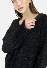 Maglione nero, peloso, con una vestibilità ampia e scollatura larga. Tessuto testurizzato con maniche lunghe, arricchito da un dettaglio di cucitura visibile.