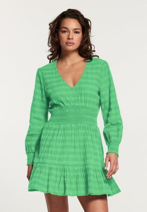Groene jurk met lange mouwen en een V-hals, voorzien van een gerimpelde taille en een gelaagde rucheszoom. Gemaakt van een gestructureerde stof met horizontale strepen.
