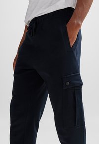 Marinblå joggingbyxor med elastisk midja, snörning, sidofickor och en cargoficka med tryckknappsdetalj.