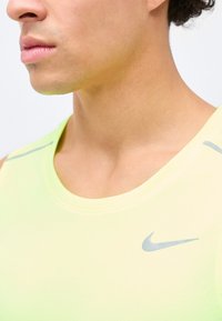 Κοντινό σε ένα άτομο που φοράει ανοιχτό κίτρινο αθλητικό αμάνικο μπλουζάκι Nike με γκρι λογότυπο Nike Swoosh στο στήθος.