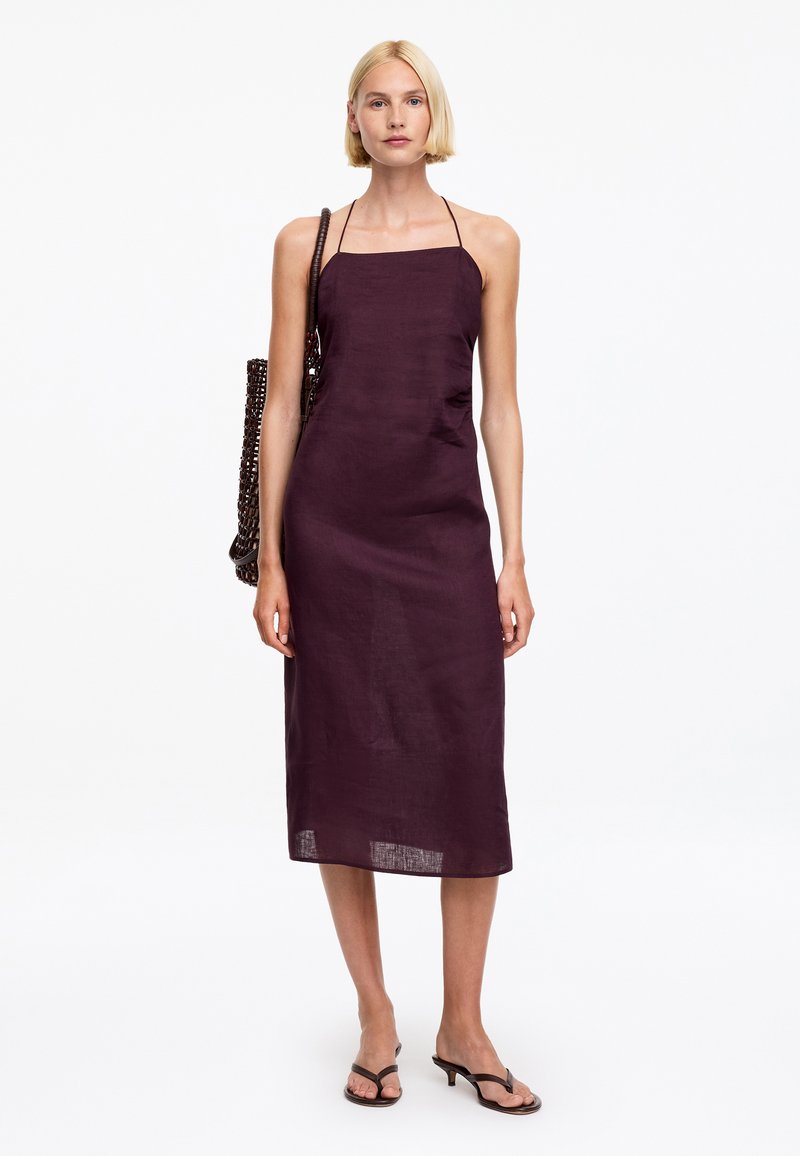 Femme portant une robe midi sans manches de couleur violet foncé, un sac à bandoulière marron foncé texturé, et des sandales à talons noires.