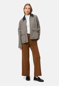 Geruit jasje met een zwarte kraag, gecombineerd met bruine wijde broekspijpen en zwarte schoenen. Voorzien van twee voorzakken.