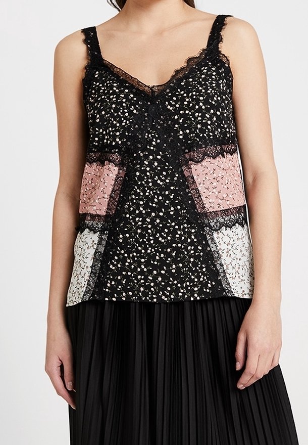 Femme portant un caraco noir orné de dentelle florale avec des panneaux à motifs rose et blanc et une jupe plissée noire.