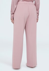 Lyserøde bukser med vide ben, glat tekstur, afslappet pasform og elastisk talje. Ingen synlige spænder eller mønstre.