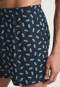 Marine boxer shorts met een elastische tailleband, versierd met een patroon van kleine, witte en teal boten op een gladde stof.