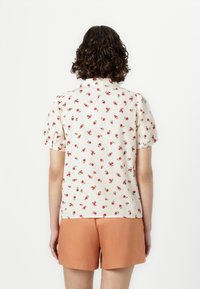 Blomstret kortermet bluse med røde roser på en kremfarget bakgrunn, med kragehals og rynkede pufferm.