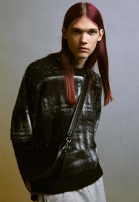 Svart, fluffig tröja med ett vitt mönster, tillsammans med en svart läderaxelväska. Väskan har en rundad form och justerbar rem.