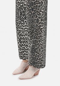 Beige semskede ankelstøvler med spids tå og et subtilt stikdesig, parret med grå leopardprint brede bukser.