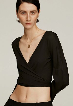 Top negro ceñido con mangas largas y escote en V pronunciado, confeccionado en una tela suave. Presenta un corte corto que revela la parte media del abdomen.