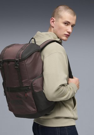 Plecak w ciemnym fiolecie i czerni, wyposażony w przednią kieszeń na suwak, regulowane paski oraz teksturowane akcenty. Wykonany z trwałej tkaniny.