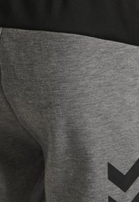Grå texturerade joggers med svart elastisk midja och en stor svart chevrondesign på nedre benet.