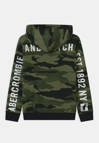 Sudadera con capucha de camuflaje en tonos verdes. Presenta texto blanco en las mangas y la espalda, con un dobladillo y puños de canalé negros. Textura de tela suave.