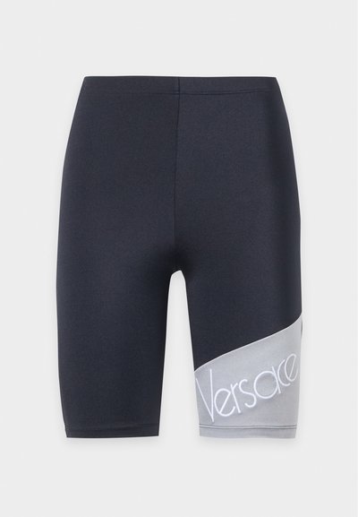 Short de sport noir longueur genou avec un panneau diagonal gris sur la jambe droite comportant un texte blanc "Versace".