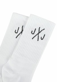 Weisse Baumwollsocken mit geripptem Textur, die ein schwarzes Logo nahe der Oberkante aufgestickt haben. Standardcrew-Längen-Design.