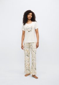 Φωτεινές μπεζ πυτζάμες με λουλουδάτο σχέδιο· το μπλουζάκι με κοντά μανίκια φέρει την επιγραφή «Always Dreaming», ενώ το παντελόνι είναι φαρδύ και έχει σχέδιο.