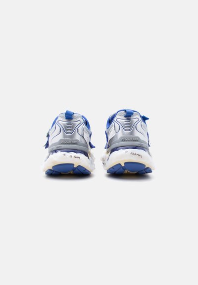 Paire de baskets de sport bleu et argent avec semelles blanches épaisses, vues de dos sur un fond neutre.