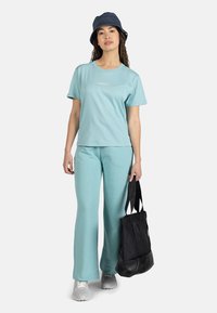 Camiseta de algodón de color azul claro y pantalones de campana a juego, combinados con un bolso tote negro y un sombrero de cubo azul marino. Presenta un diseño sencillo y una textura suave.