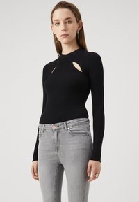 Svart ribbade långärmade topp med utskärningar, kombinerad med ljusgrå tajta jeans. Slät textur, kroppsnära design.
