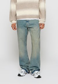 Light blue straight-leg jeans with a faded texture and slight distressing, paired with white sneakers featuring grey accents.