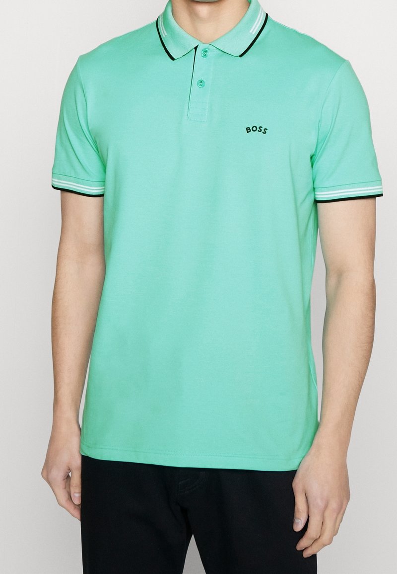 Ljusgrön polo skjorta med svart och vit randig krage och mudd. Har tre knappar vid halsen och en liten svart logotyp på bröstet.