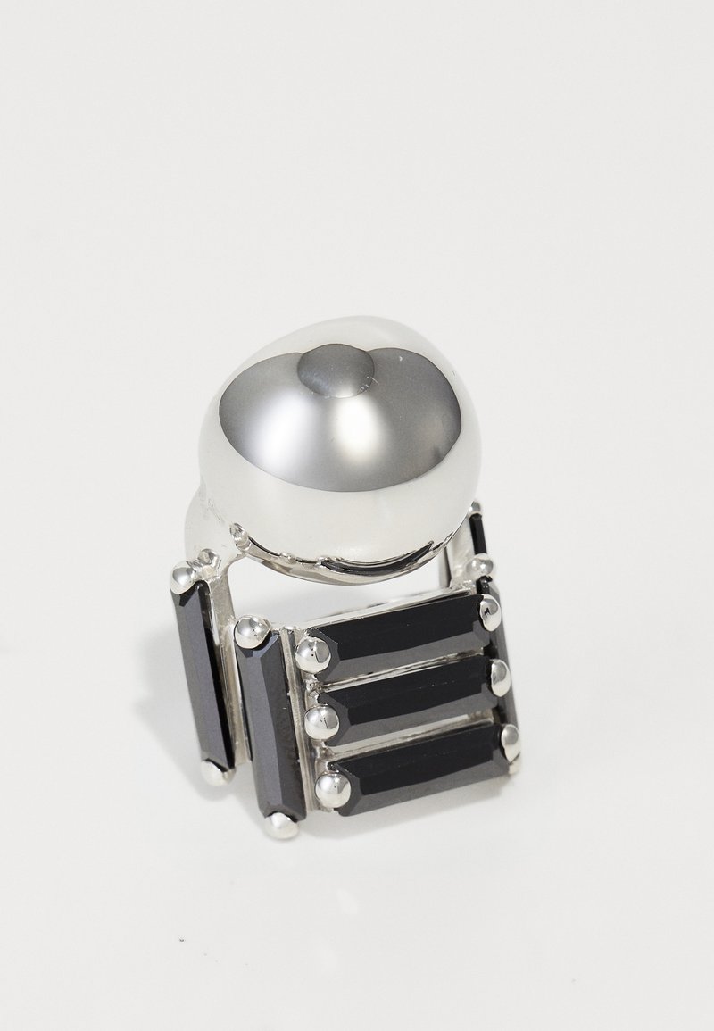 Ezüst állítmányú gyűrű, kerek, sima kupolával és három téglalap alakú fekete kővel, fém díszítésekkel és tüskékkel rögzítve.