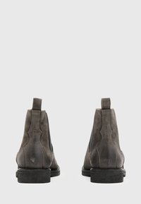 Botas Chelsea de ante gris con paneles laterales elásticos, que presentan una puntera redondeada y un tacón bajo apilado. Sutil marca en la parte trasera.