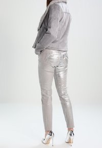 Harmaa mokkavillapuku, jossa on tekoturkiskaulus, yhdistettynä kiiltäviin hopeisiin metallihousuihin ja hopeisiin korkokenkiin. Sujuva pinta ja istuva muotoilu.