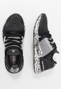 Zapatillas deportivas en negro y gris con una parte superior de tejido texturizado, acentos de estampado de serpiente en patrón y una suela de goma resistente. Diseño con cordones.
