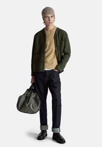 Zelený vlněný kardigan, béžová košile, tmavé džíny, šedá taška, černé boty. Texturovaná látka, zapínání na knoflíky, vyhrnuté rukávy, jemné designové detaily.