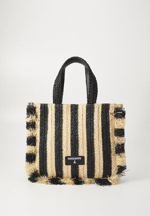 Τσάντα tote από υφαντό υλικό με μαύρες και φυσικές ψάθινες ρίγες, υφή με υφή, φούντες στην άκρη και πλεχτούς μαύρους λαβές. Έχει ετικέτα με λογότυπο.