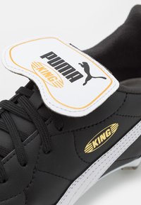 Crne kožne fudbalske kopačke s bijelim detaljima. Sadrži zlatni logo "KING" i naziv brenda "PUMA" na bijelom oznaci. Teksturalna površina. Dizajn sa vezicama.