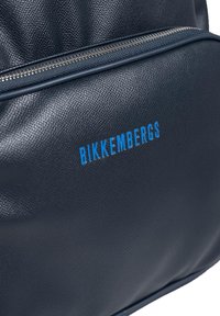 Bikkembergs marineblå læderrygsæk med en tekstureret overflade, sølv lynlås og blåt logo, der står frem på forsiden.