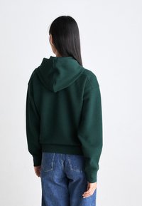 Grønn kortermet hettegenser med myk tekstur og avslappet passform. Kombinert med lyseblå høye jeans.