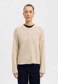 Beige wool cardigan with a round neckline, long sleeves, and six buttons down the front. Soft texture and cropped design.