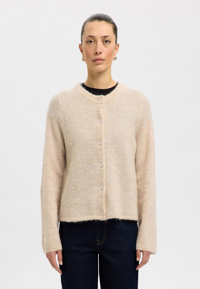 Beige wool cardigan with a round neckline, long sleeves, and six buttons down the front. Soft texture and cropped design.