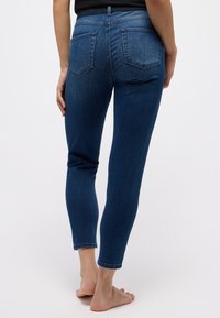Schlanke Jeans aus dunkelblauem Denim mit einer mittelhohen Taille, fünf Taschen und einer glatten Textur, die über dem Knöchel endet.
