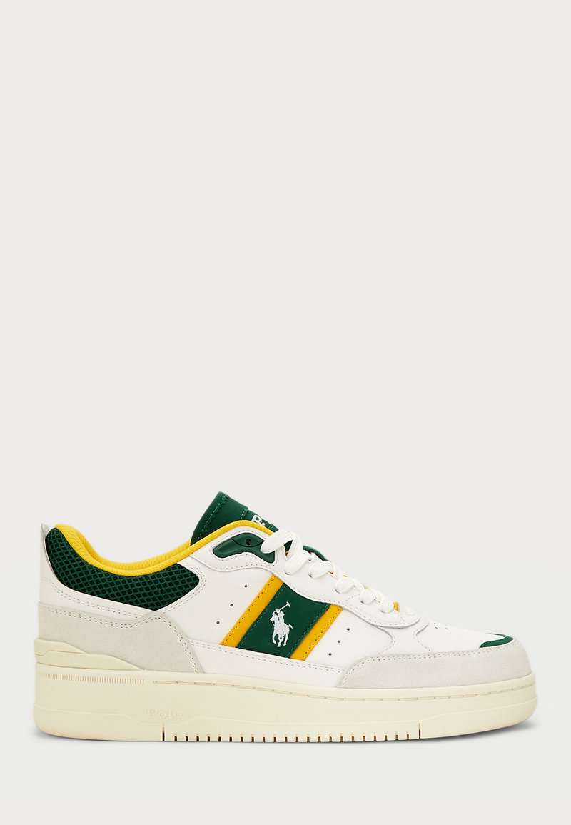Λευκά αθλητικά παπούτσια με πράσινες και κίτρινες λεπτομέρειες, πάνελ από διχτυωτό υλικό και σουέτ μύτη. Ο σχεδιασμός περιλαμβάνει λογότυπο στο πλάι και παχιά σόλα.