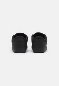 Black sneakers feature a smooth exterior with a padded collar and textured heel. The sole is flat and minimal, enhancing a sleek design.