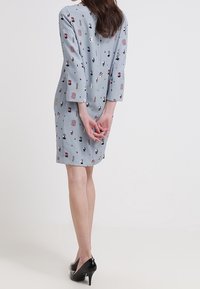 Jasnoniebieska sukienka o subtelnym wzorze, z rękawami do trzech ćwierci i prostym kroju, zestawiona z czarnymi szpilkami.