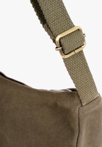 Adjustable olive green fabric shoulder strap with brass buckle attached to a matching olive green canvas bag corner.