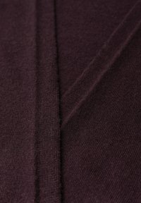 Bordowy materiał dzianinowy o miękkiej teksturze, z centralnym szwem i delikatnymi liniami ukośnymi, tworzącymi smukły design.